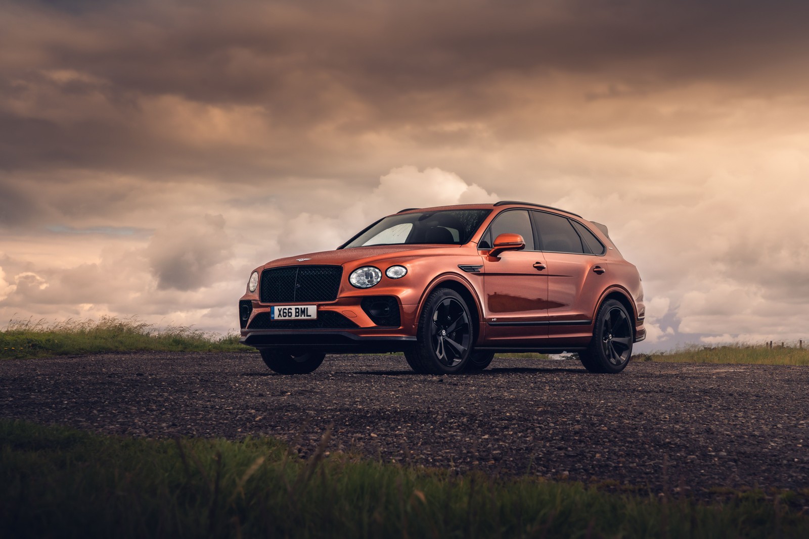 Um suv vermelho estacionado em uma estrada de cascalho sob um céu nublado (bentley bentayga v8, 8k, primeira edição, 2020, 5k)