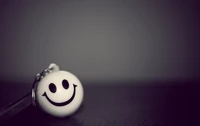 A close-up of a cheerful smiley face keychain against a dark, softly blurred background, radiating happiness and positivity.