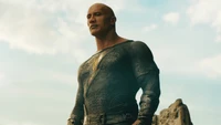 Dwayne Johnson als Black Adam, der in einer kraftvollen Pose gegen einen dramatischen Himmel steht.