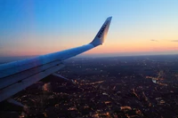 Vista do pôr do sol da asa do avião sobre uma paisagem urbana