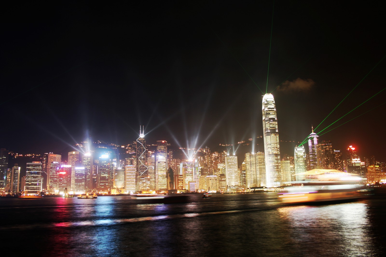 Visão aérea do horizonte da cidade à noite com um barco em primeiro plano. (victoria harbour, uma sinfonia de luzes, arranha céus, atração turística, noite)