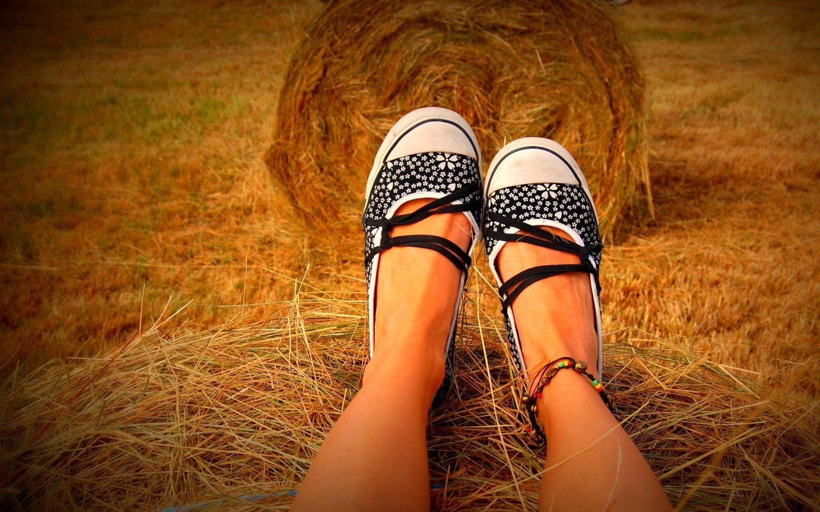 Someone is sitting on a hay bale with their feet up (human leg, shoe, foot, girl)