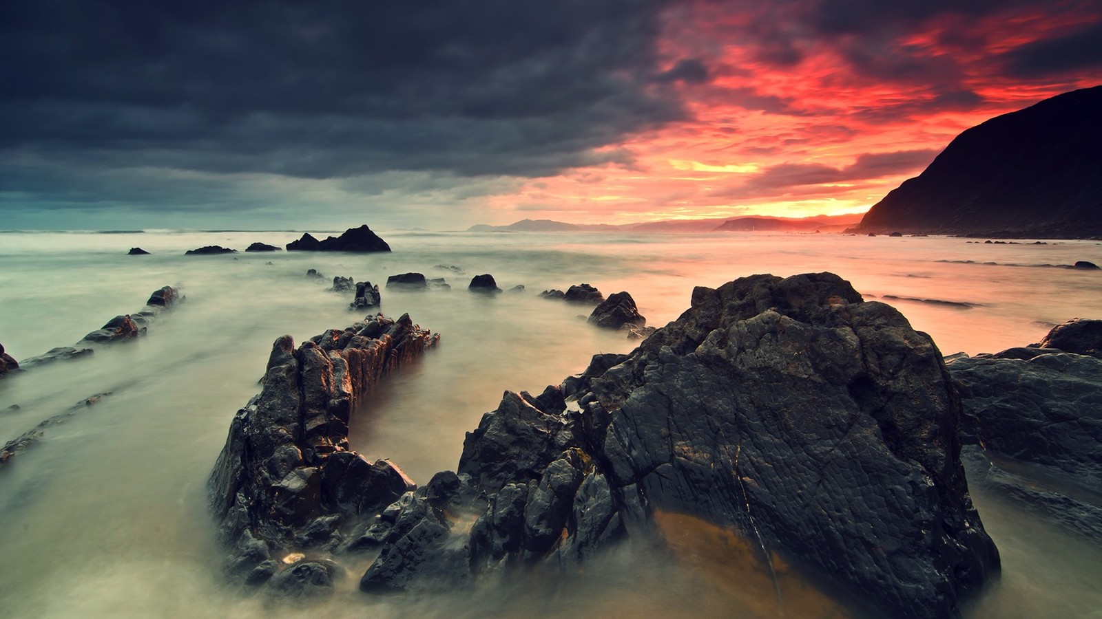 A long exposure photograph of a sunset over the ocean with rocks in the foreground (sea, rock, coast, shore, ocean)