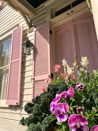 Encantadora puerta rosa adornada con flores vibrantes, entrada acogedora a un hogar elegante.