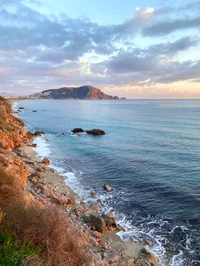 Costa serena ao crepúsculo com águas azuis e horizonte montanhoso