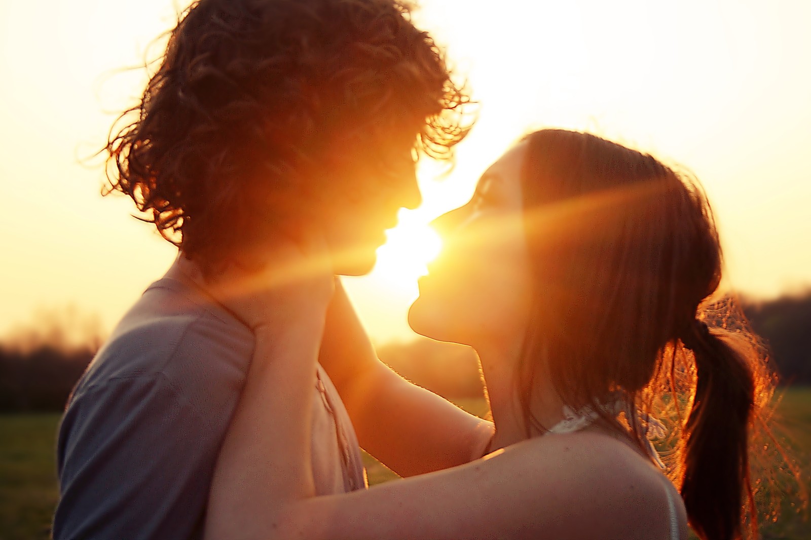 There is a man and woman that are standing in a field (romance, couple, kiss, people in nature, backlighting)