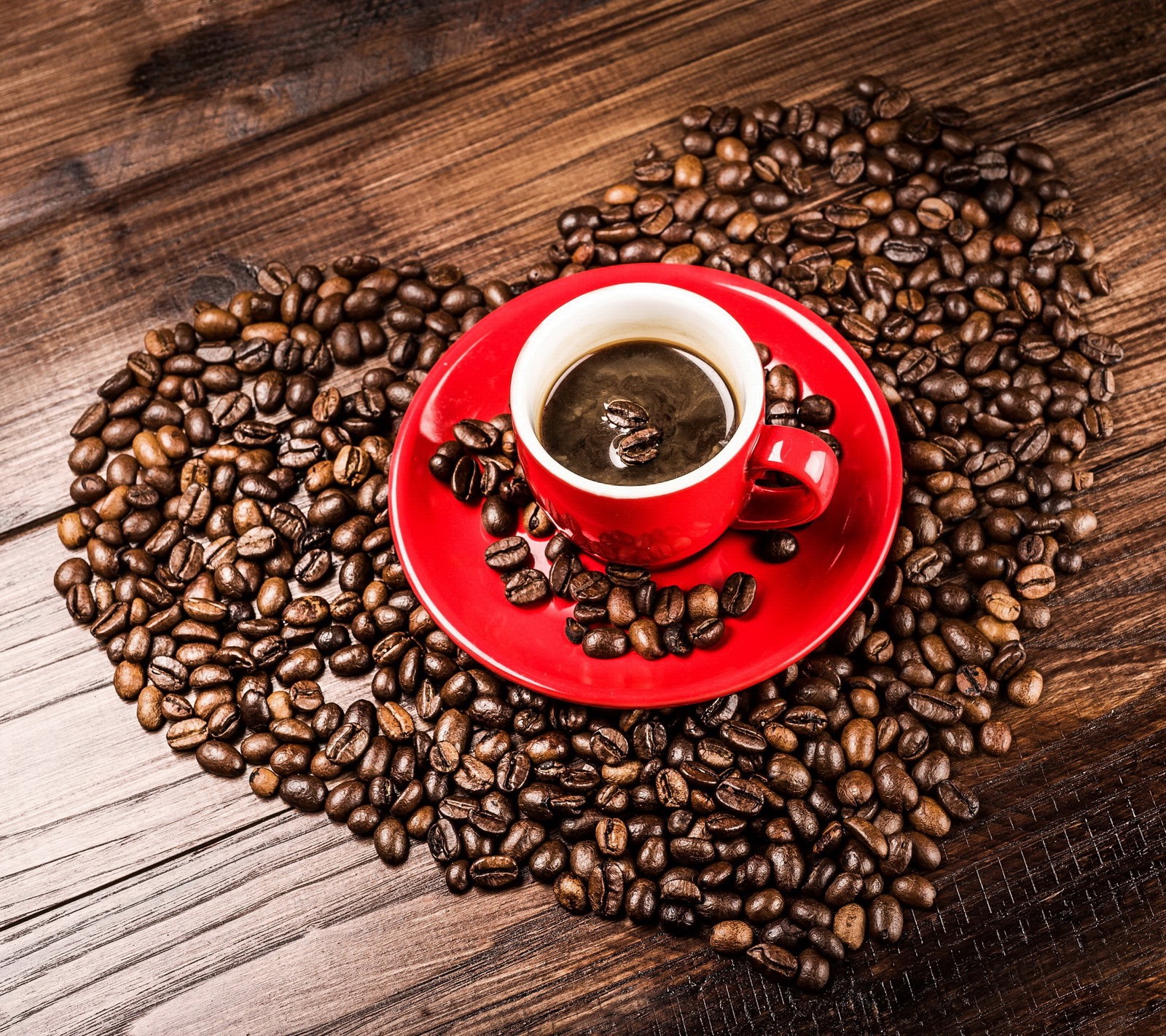 Um close-up de uma xícara de café vermelha em uma mesa com grãos de café (feijões, café, xícara, coração, amor)