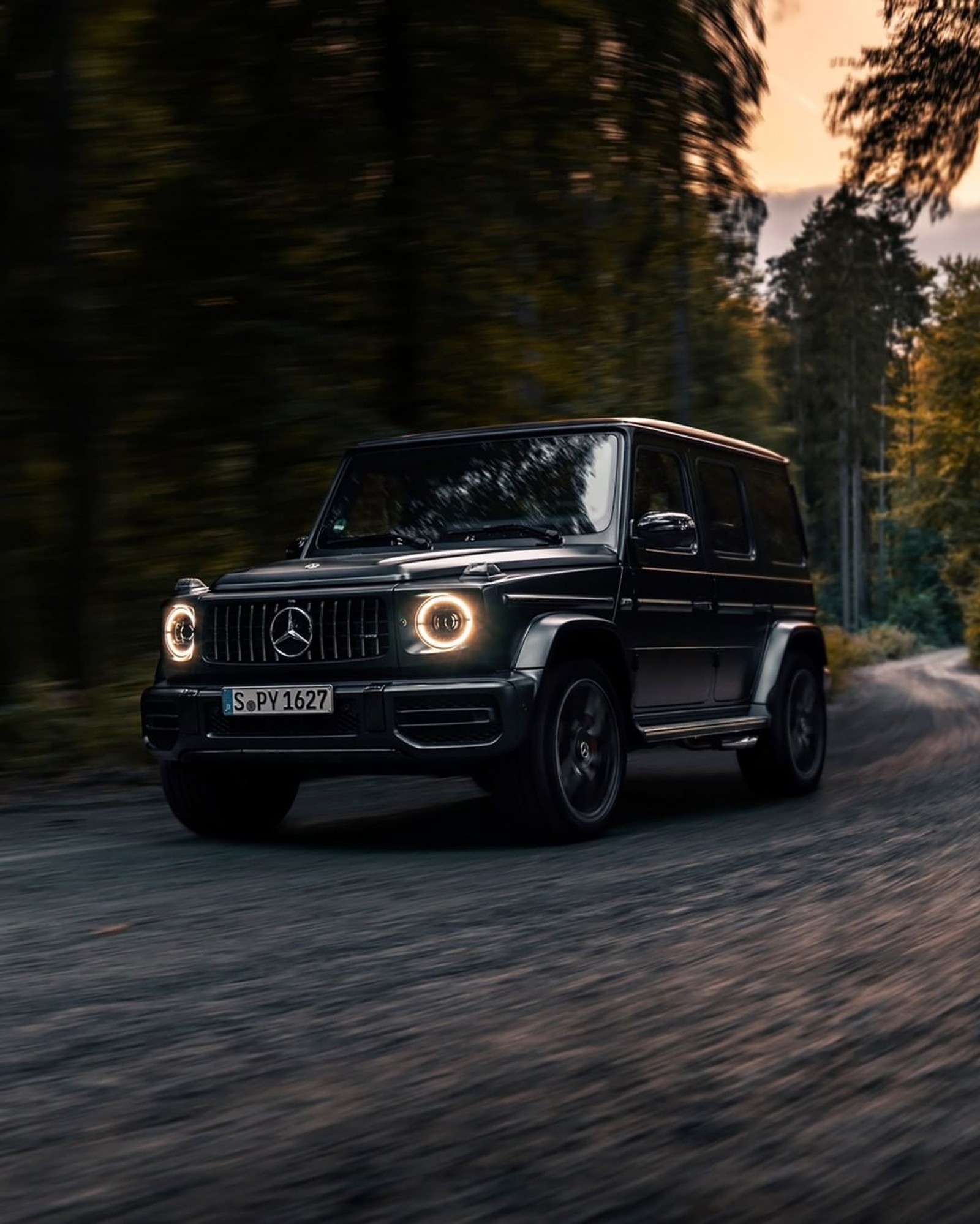 A black mercedes g - class driving down a road in the evening (black, car, class, hd, mercedes)