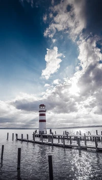 Torre de farol vermelha e branca contra um céu cinza dramático