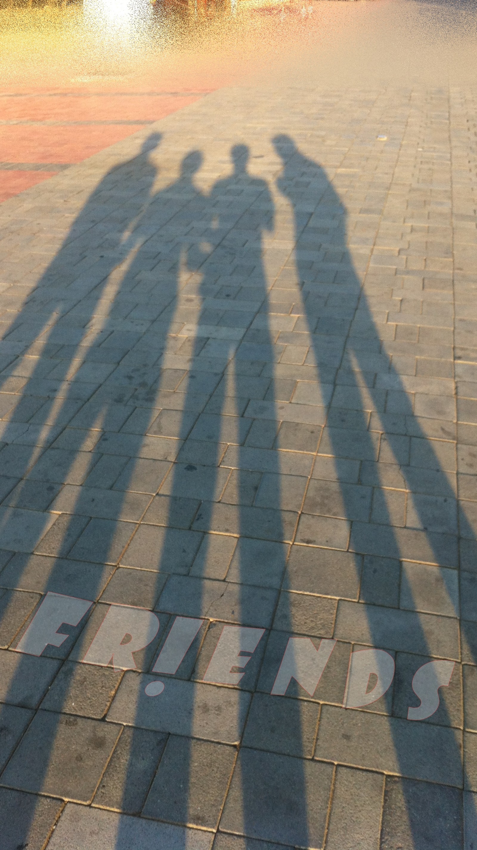 Shadows of two people standing on a brick sidewalk with the word paris written on it (frend, friend)