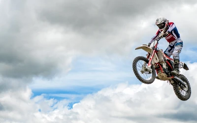 A motocross stunt performer soaring through the sky on a motorcycle against a backdrop of dramatic clouds.