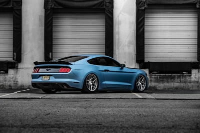 Eleganter blauer Ford Mustang mit stylischen Leichtmetallrädern vor urbanem Hintergrund geparkt.