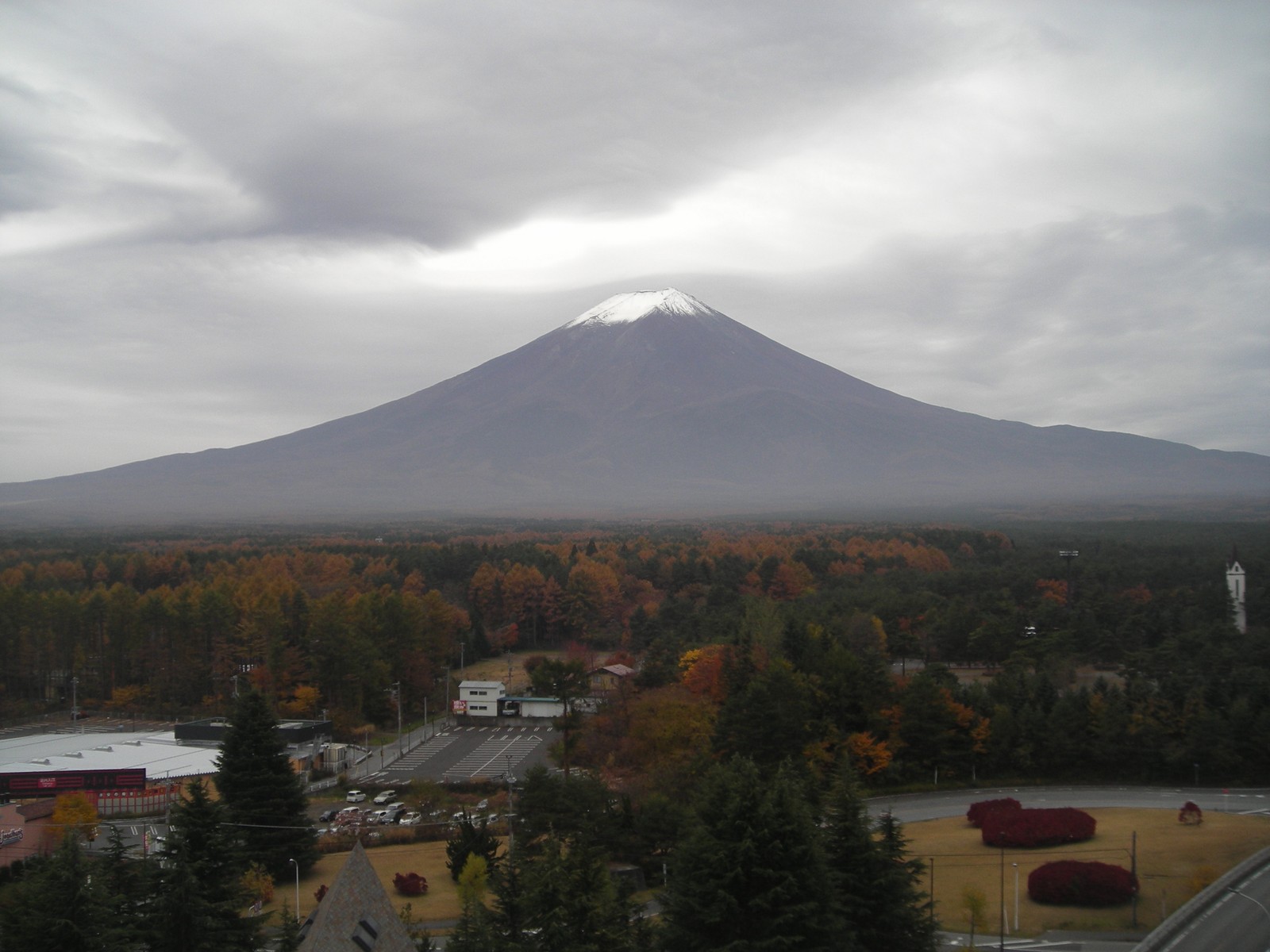 Un vue arqué d'une montagne au loin avec une route et un parking (stratovolcan, décor montagnard, hauts plateaux, chaîne de montagnes, volcan)