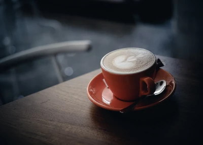 Cappuccino con intrincado arte latte en una vibrante taza naranja sobre una mesa de madera.