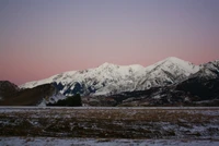 Schneebedeckte Berge in der Dämmerung, mit einer ruhigen Winterlandschaft und einem Hauch von rosa Himmel.