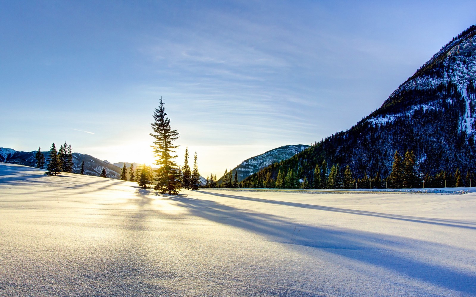 Uma vista de um campo coberto de neve com árvores e montanhas ao fundo (neve, inverno, natureza, nuvem, árvore)