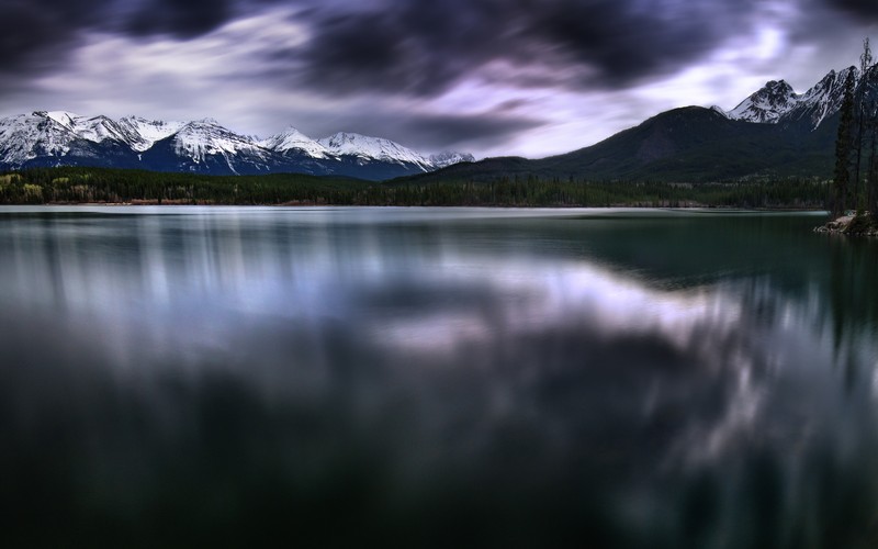 Горы отражаются в воде озера под облачным небом (pyramid lake, канада, темные облака, пейзаж, длительная выдержка)