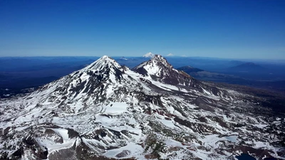 Schneebedeckte Stratovulkane erheben sich majestätisch gegen einen klaren blauen Himmel und zeigen die raue Schönheit der bergigen Landschaft in Oregon.