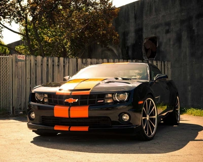 Chevy Camaro preto com listras laranjas estacionado em um ambiente urbano.