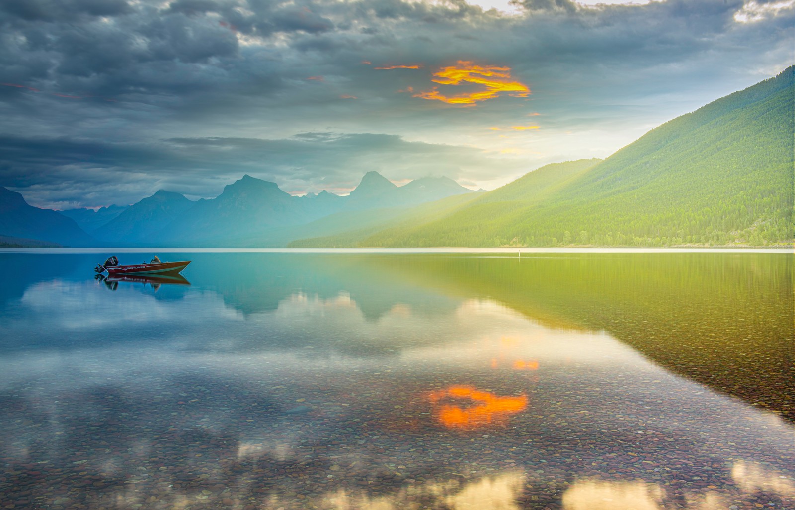 Uma imagem desfocada de um barco em um lago com montanhas ao fundo (lago mcdonald, parque nacional glacier, montana, nascer do sol, hora dourada)