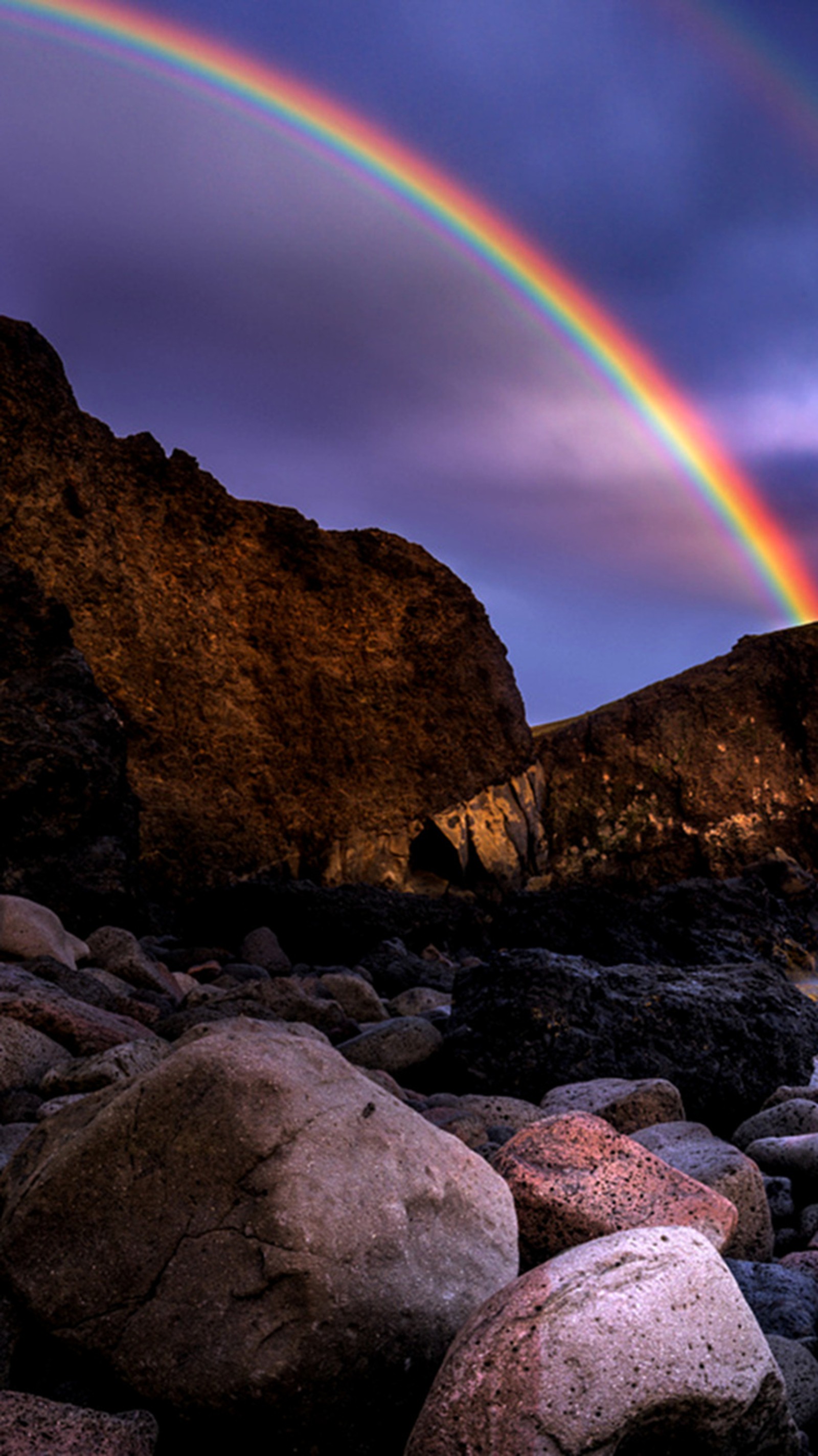 There is a rainbow that is shining over a rocky beach (beach, majestic, rainbow)