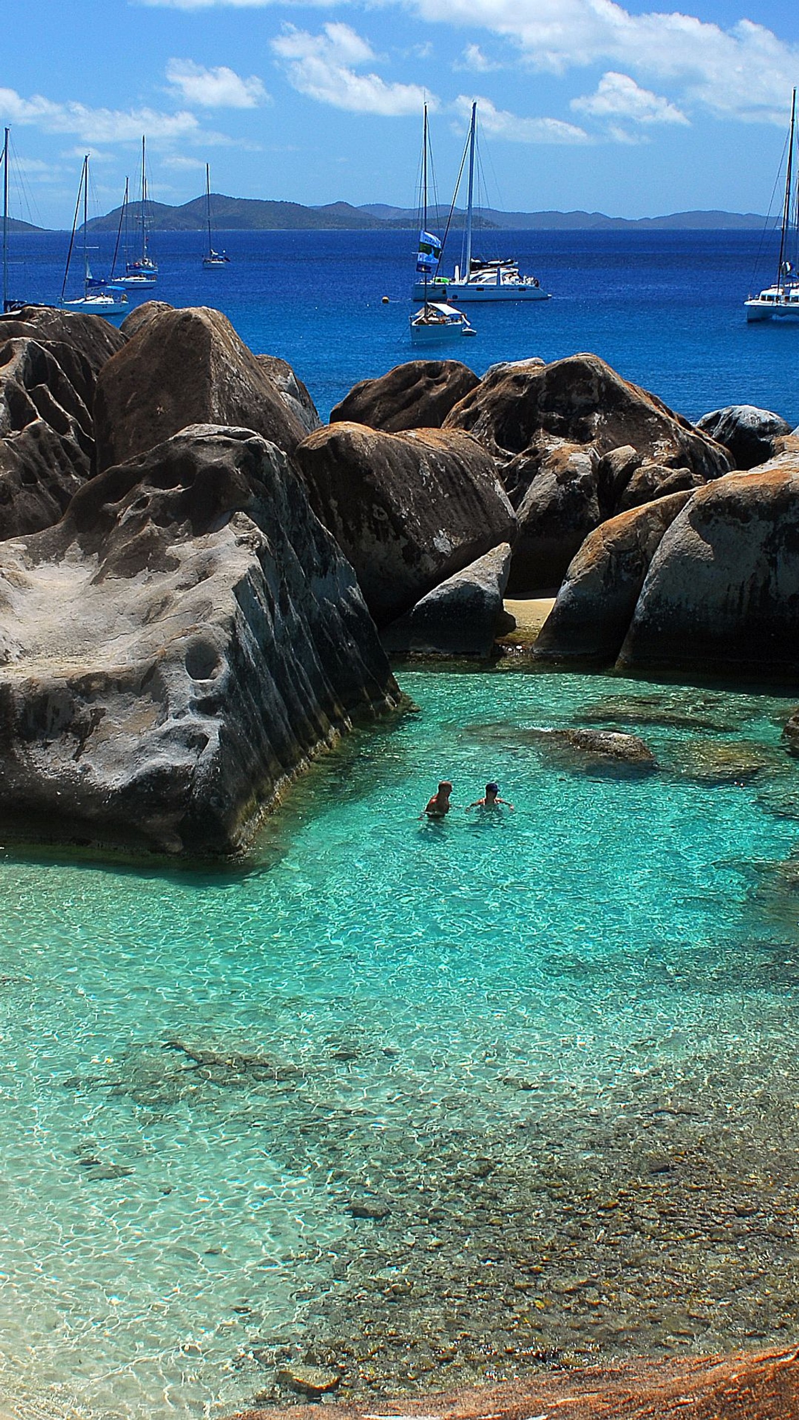 Há muitos barcos na água perto de uma praia rochosa (caribbean coast, sail boats, shore rocks)