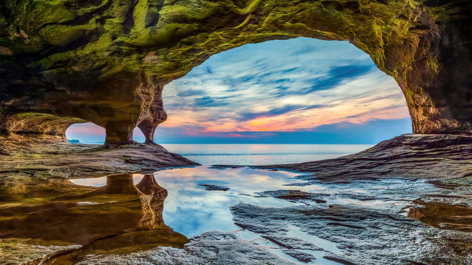 Uma vista de uma caverna com um pôr do sol ao fundo (praia, nascer do sol, rochas, litoral nacional, cenário)