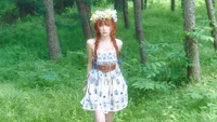 Seulgi avec une couronne de fleurs, portant une robe à motifs, marchant à travers une forêt verdoyante.