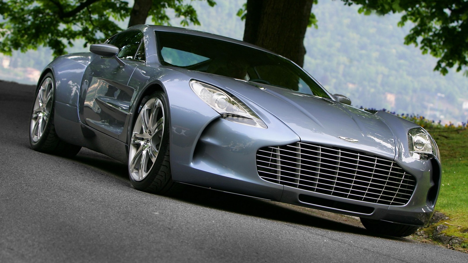 A close up of a silver car driving down a road (aston martin, car, sports car, supercar, rim)