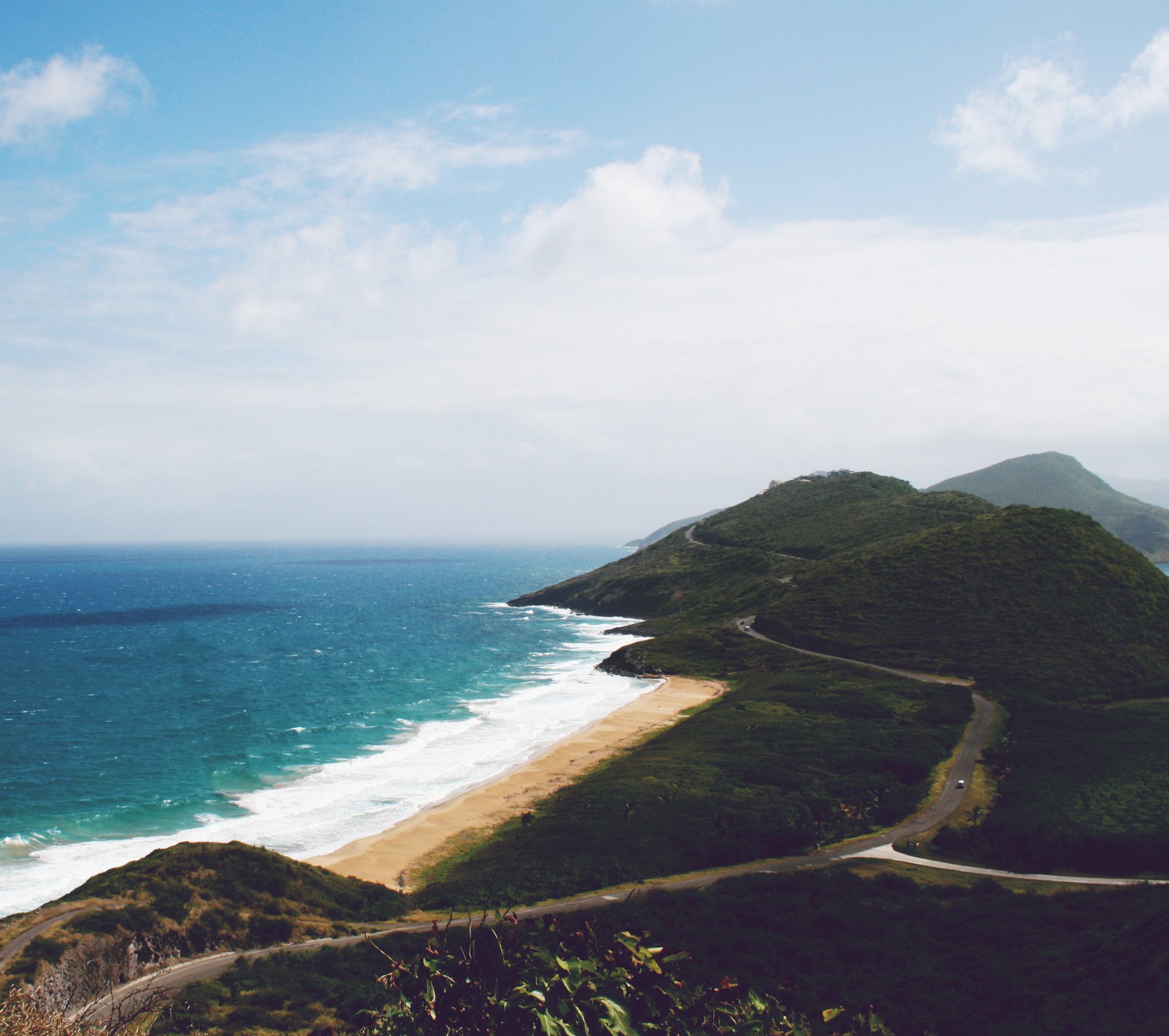 Vista aérea de uma estrada sinuosa ao longo do oceano com uma praia ao fundo (bonito, havai, viagem, férias)