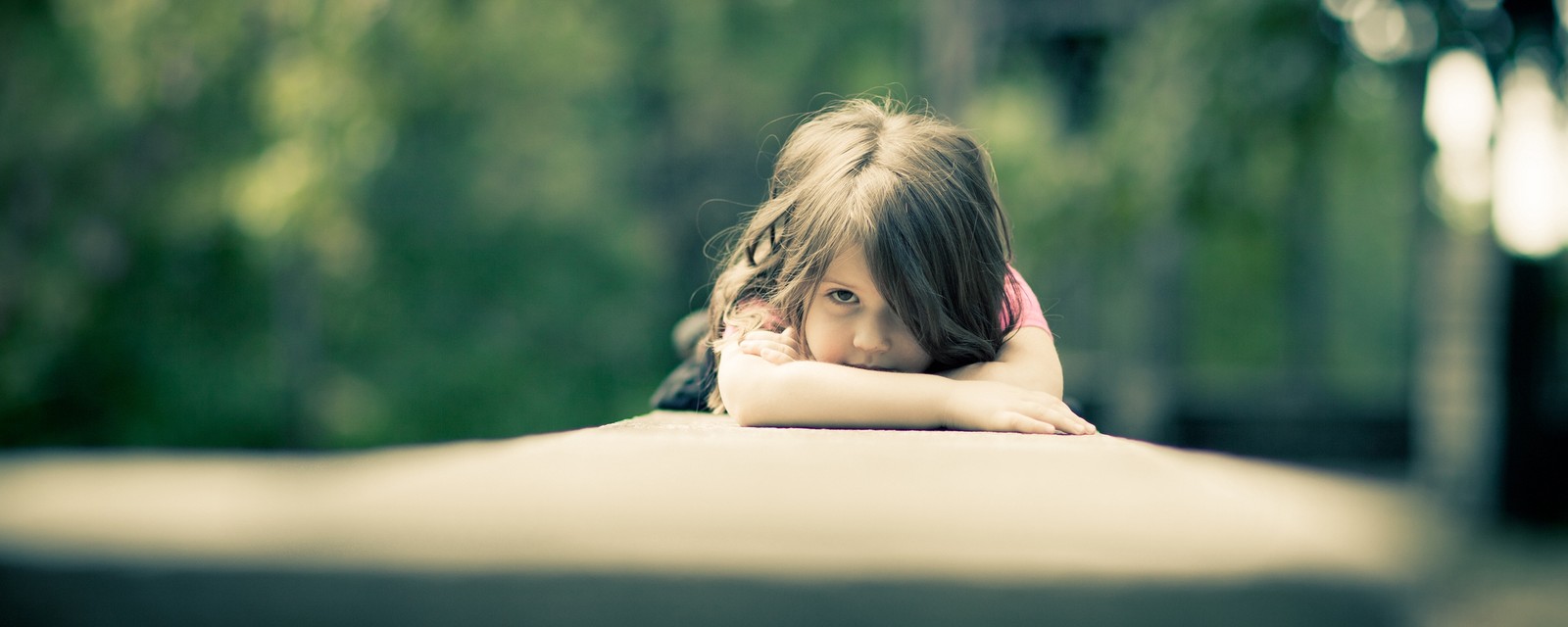 There is a little girl that is leaning on a ledge (skin, grass, girl, green, eye)