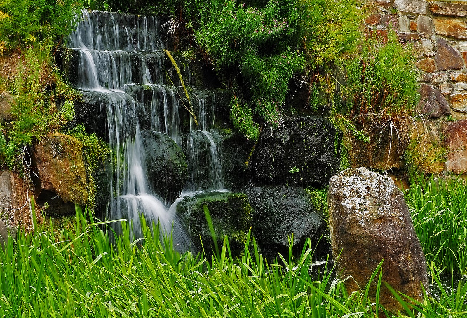 Hay una cascada que cae por una colina con rocas (naturaleza, cauce, cascada, agua, recursos hídricos)