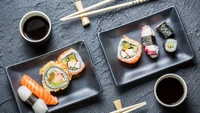 Leckere Auswahl an Sushi-Rollen, serviert auf eleganten schwarzen Tellern, begleitet von Sojasauce und Essstäbchen, die die Kunst der japanischen Küche zeigen.