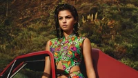 Selena Gomez en un vibrante atuendo floral junto a un auto vintage contra un fondo exuberante.