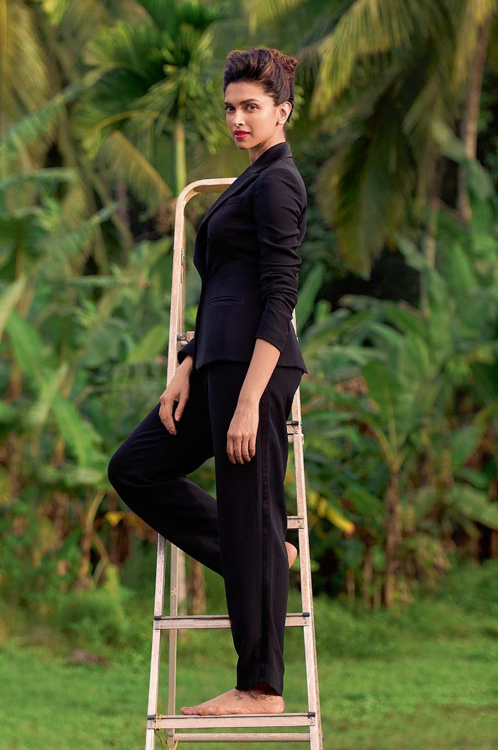 Woman in black suit standing on a ladder in a field (actress, apple, bollywood, deepika, diva)