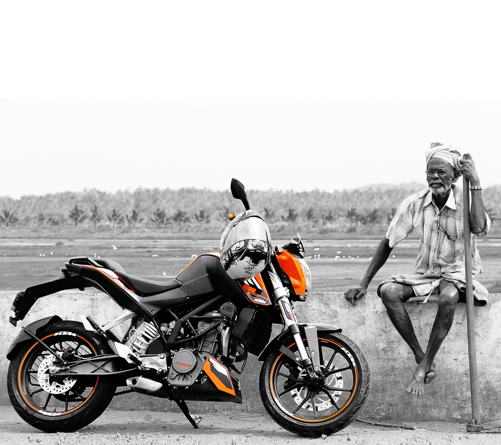 Há um homem sentado em uma pedra ao lado de uma motocicleta (bicicleta, duque, hd, índia, india)