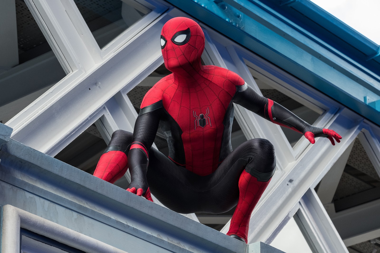 Spider-man assis sur un rebord dans un costume sur un pont (disney, loin de chez soi, marvel, mcu, rouge et noir)