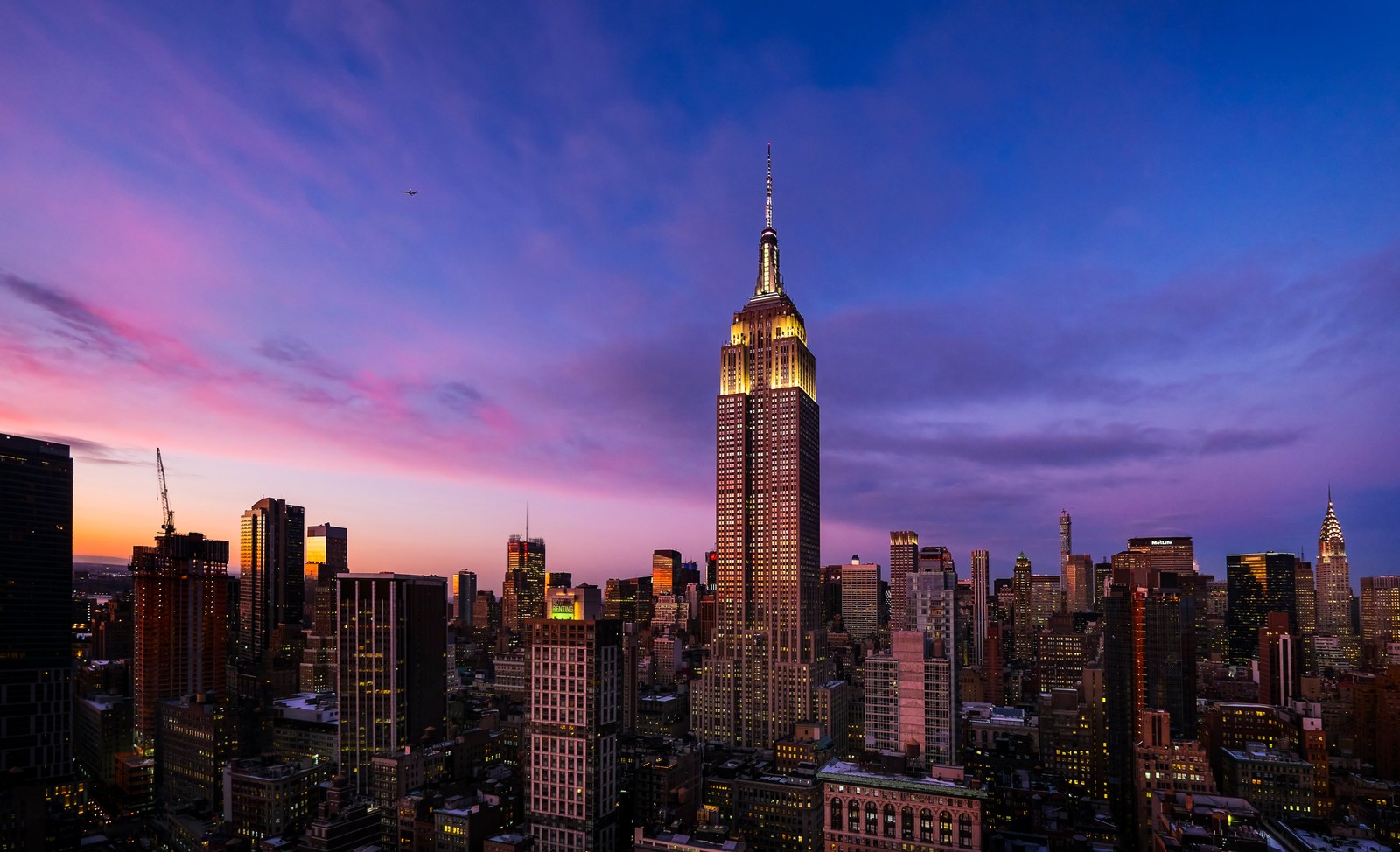 Una vista del horizonte de una ciudad con un edificio alto iluminado por la noche (empire state building, noche, nueva york, new york city, crepúsculo)