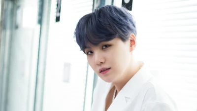 Min Yoongi (Suga) do BTS, com cabelo azul estiloso e um traje branco, olha pensativo.