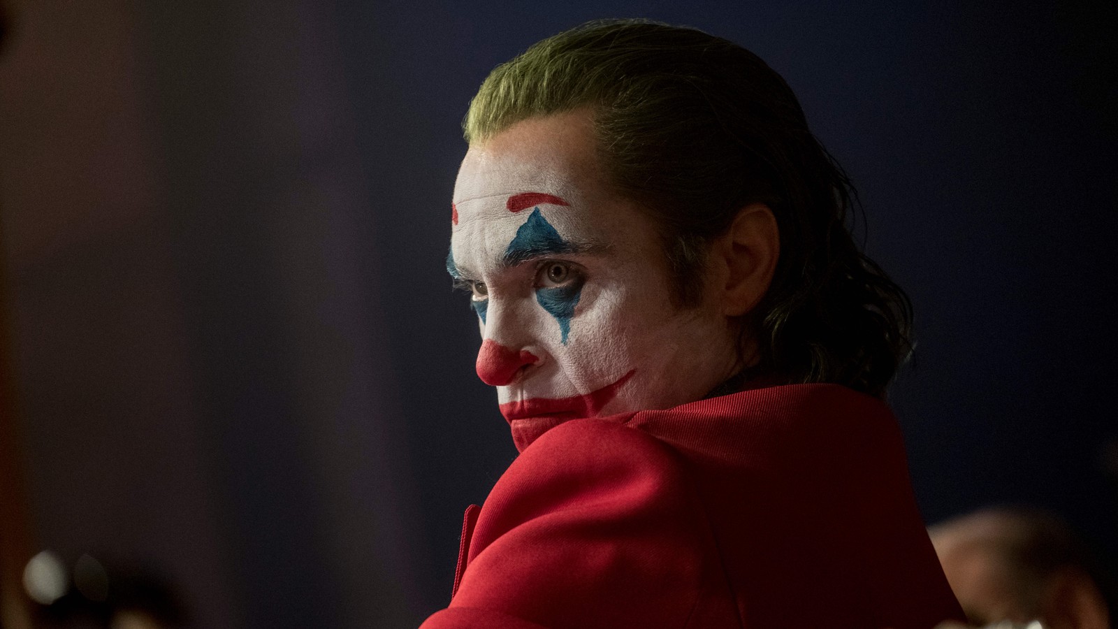 Un joker en veste rouge avec un visage peint en bleu et des cheveux verts (joker 2019, film, joker, joaquin phoenix)