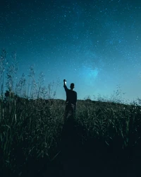 Silhouette of a person standing in grass under a starry night sky