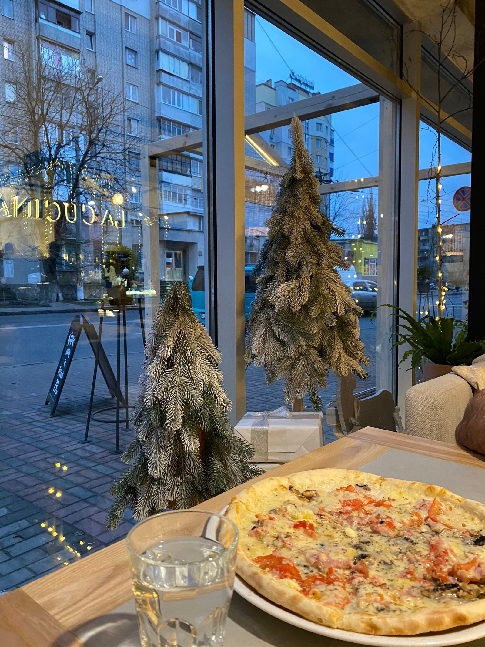 Hay una pizza en un plato sobre una mesa frente a una ventana (árbol, ramo, pizza, comida, productos horneados)