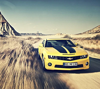 Желтый Chevrolet Camaro на rugged грунтовой дороге с гористым ландшафтом на заднем плане.