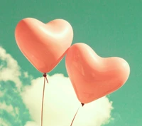 Two pink heart-shaped balloons floating against a serene sky with fluffy clouds.