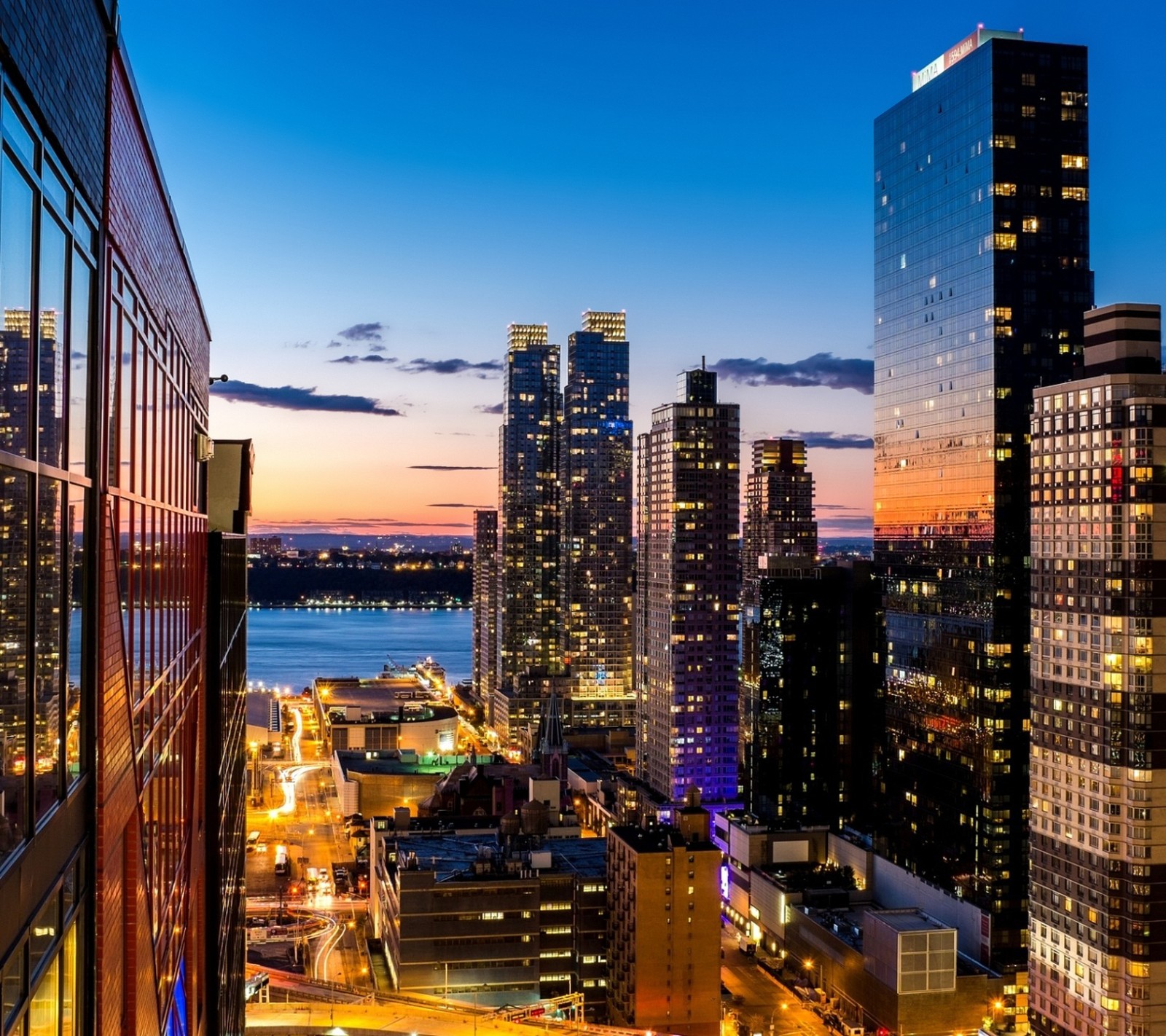 Uma vista de uma cidade à noite com um rio ao fundo (edifício, cidade, nova york, new york, ny)