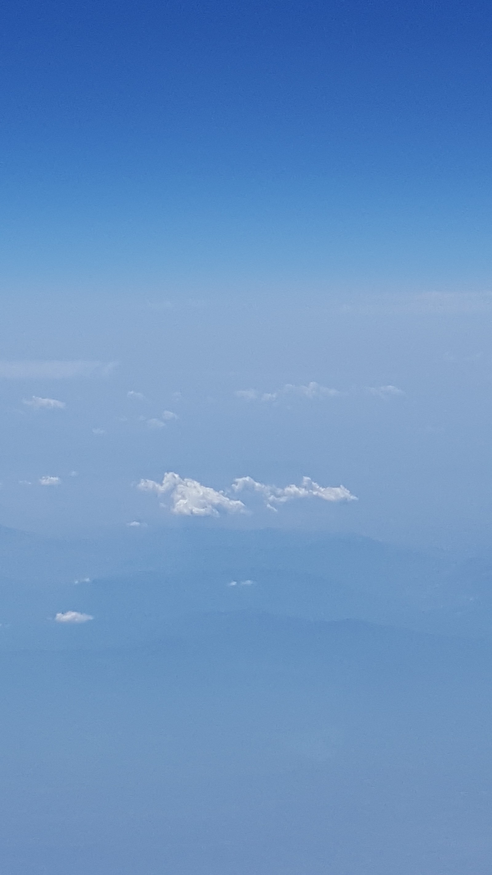 Vue aérienne d'un avion survolant une chaîne de montagnes (bleu, nuages, terre, montagnes, scattered)