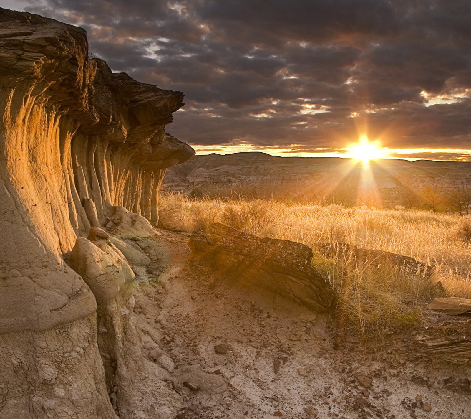 Arafed rock formation in the desert with sun setting in the background (clouds, mountains, rock, sunset)