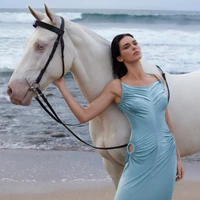 Kendall Jenner in einem fließenden blauen Kleid posiert mit einem weißen Pferd am Strand während eines beeindruckenden Fotoshootings.