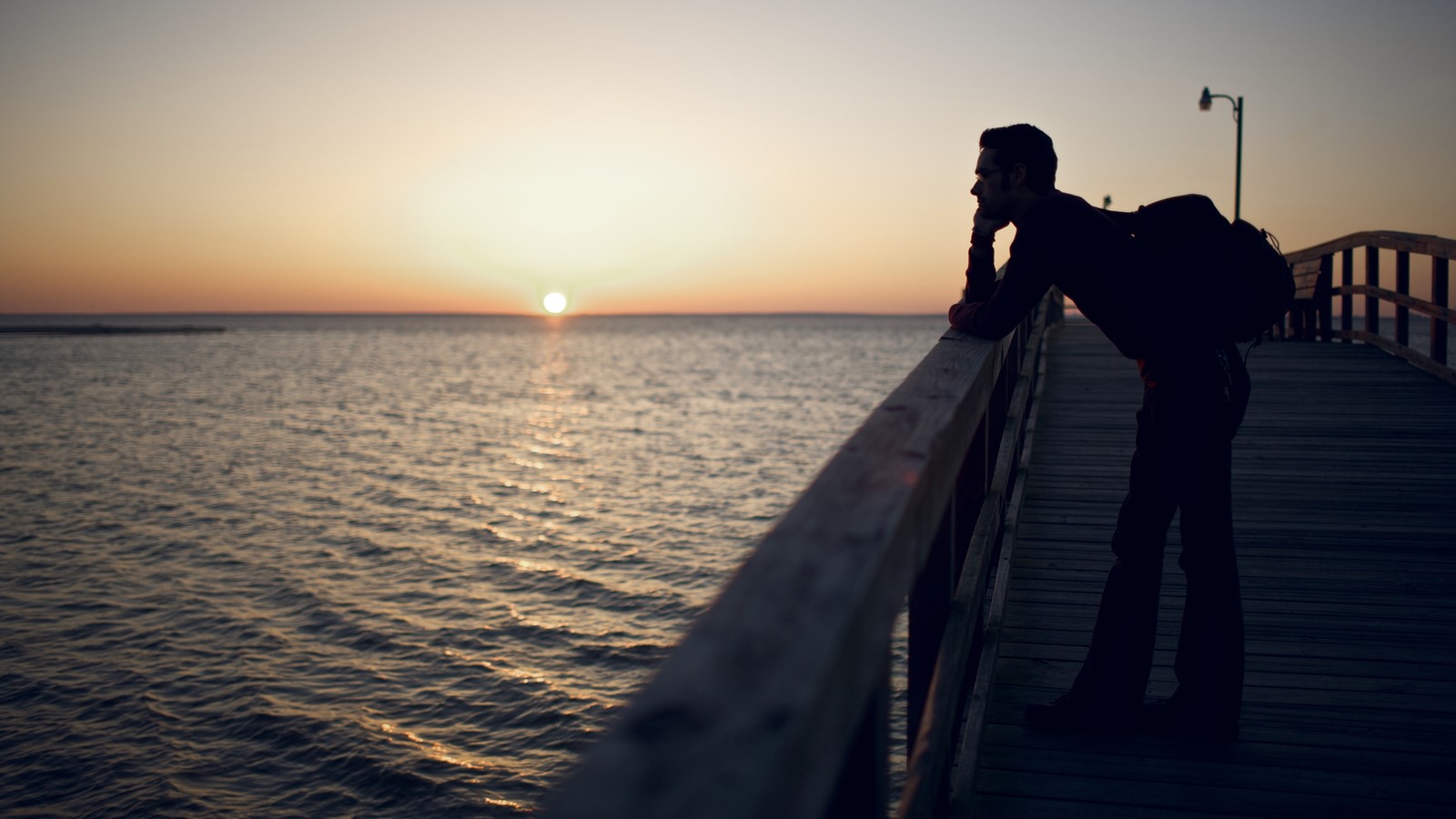 Il y a un homme sur un quai regardant le coucher de soleil. (eau, horizon, mer, océan, coucher de soleil)