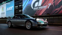 Um Mazda RX-7 elegante estacionado sob painéis publicitários vibrantes no ambiente de corrida dinâmico de Gran Turismo 7.